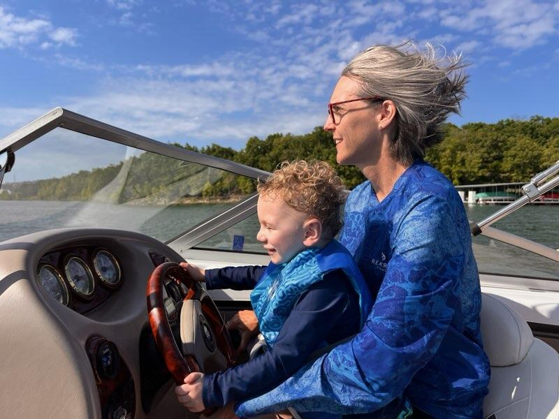 Jen Shenberger holding a child in her lap while driving a boat, wind blowing through her hair